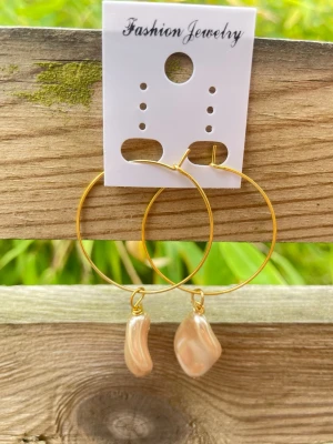 Guldfärgade hoops med beige pärlor - Stora hoops i guldfärgad metall med oregelbundna, skimrande pärlor i beige nyans. Snygg och trendig design som ger en unik touch till din stil. Perfekta för dig som gillar statementörhängen och vill sticka ut lite extra. Total längd är 55 mm