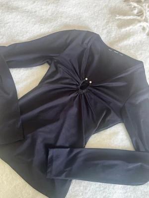 Svart långärmad topp med pärldetalj passar 2000s stilen - Snygg svart långärmad topp med v-ringning och en liten cut-out framtill som pryds av två pärlor. Figurnära passform och stretchigt material som ger en smickrande siluett. Perfekt att styla med jeans eller kjol för en trendig look. skicka gärna prisförslag🥹