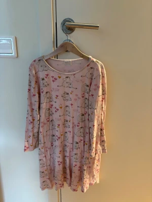 Rosa Mumin nattlinne med tryck - Sött rosa nattlinne från Moomin med gulligt Mumin-tryck och små hjärtan och blommor. Långärmad modell i mjukt material, perfekt för mysiga kvällar. Rund halsringning och avslappnad passform.