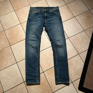 Blå jeans från Nudie Jeans - Säljer ett par snygga blå jeans från Nudie Jeans i bra skick. De har en klassisk femficksdesign och en bekväm passform. Helt nya, skick 10/10, storlek 30/32 hör av er vid funderingar!