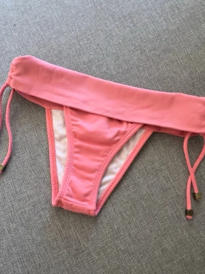 Rosa bikiniunderdel med snörning - Snygg bikiniunderdel från Brasilien i ljusrosa med bred linning och snörning i sidorna. Bikinitrosan har en enkel och stilren design.  Perfekt för lata dagar på stranden eller poolen. #bikini