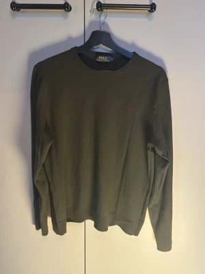 Olivgrön tröja från Polo Ralph Lauren - Olivgrön långärmad tröja från Polo Ralph Lauren med rund halsringning och diskret broderad logga på bröstet. Tröjan är 10/10 skick, och passar perfekt nu till hösten när det börjar bli lite kallare ute! Priset kan diskuteras vid snabb affär!