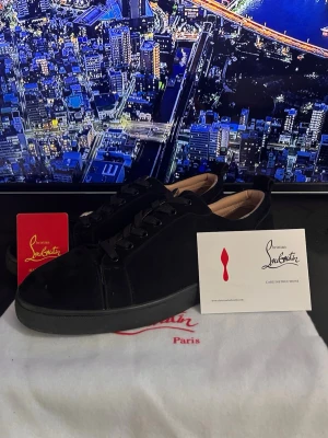 Loubs - Snygga svarta sneakers från Christian Louboutin i mocka med klassisk röd sula. Skorna har svarta. Perfekta för dig som vill ha en exklusiv och stilren look med en ikonisk touch.