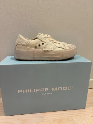 Vit/Beige sneakers från Philippe Model - Säljer ett par vita/ beige sneakers från Philippe Model i denim med slitna detaljer. Knappt använda men lite slitna. Kommer med originallådan och skopåse.