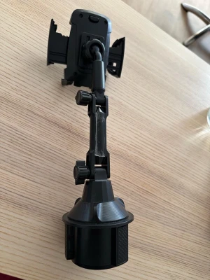 Justerbart mobilhållare till bil - Säljer en svart mobilhållare för bilen som monteras i mugghållaren. Hållaren har justerbara armar och flexibel arm med flera leder för optimal vinkel. Tillverkad i plast och gummi för bra grepp om mobilen. Perfekt för navigation eller handsfree-användning.
