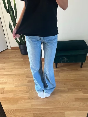 Ljusblå bootcut jeans - Säljer ett par ljusblå jeans med bootcut passform och hög midja. Jeansen har klassiska fickor fram och bak samt raka ben som blir vidare nedtill. Perfekta för en avslappnad och trendig look.