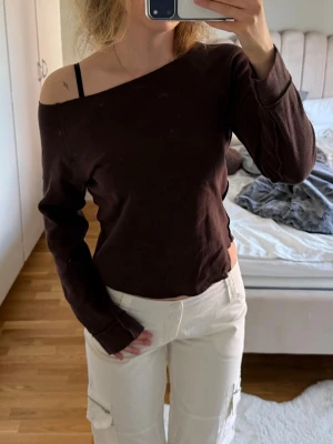 Mörkbrun offshoulder långärmad topp - Säljer en mörkbrun långärmad topp med offshoulder-design. Toppen har en avslappnad passform och är tillverkad i ett mjukt bomullsliknande material. Perfekt för dig som gillar en enkel men ändå trendig stil. Obs! Lite nopprig 