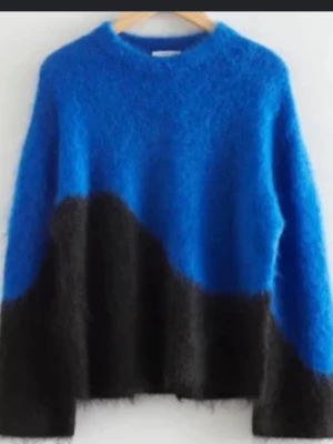 Blå och svart fluffig stickad tröja - Cool stickad tröja i blått och svart med oversized passform och rund hals. Tröjan har en mjuk, fluffig yta och ett vågigt färgblocksmönster. Perfekt för dig som vill ha en statement piece i garderoben.
