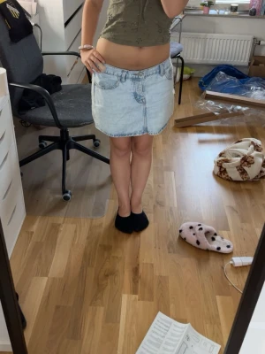 Ljusblå jeanskjol med fickor - Säljer en ljusblå jeanskjol i kort modell med klassiska fickor både fram och bak. Kjolen har en avslappnad passform och är tillverkad i denim, perfekt för en casual look. Passar till många olika stilar och är enkel att matcha.