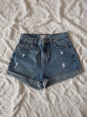 FB Sister jeansshorts med hög midja – stl M - Säljer ett par ljusblå högmidjade jeansshorts från FB Sister. Shortsen har slitna detaljer, uppvikta benslut och klassisk femficksdesign. Perfekta för varma dagar och ger en avslappnad vibe till din outfit.