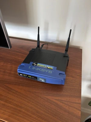 Linksys trådlös router med antenner - Säljer en klassisk Linksys trådlös router i svart och blå plast med två antenner för bättre räckvidd. Perfekt för dig som vill ha stabilt wifi hemma eller på kontoret. Enkel att koppla in och använda till flera enheter.