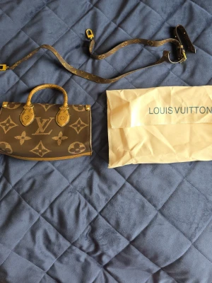 Louis Vuitton Monogram handväska - Snygg brun handväska från Louis Vuitton med klassiskt monogrammönster i beige och guldiga detaljer. Väskan har två handtag och avtagbar axelrem, perfekt för dig som gillar lyxig och tidlös design. Materialet är tåligt canvas med läderdetaljer.