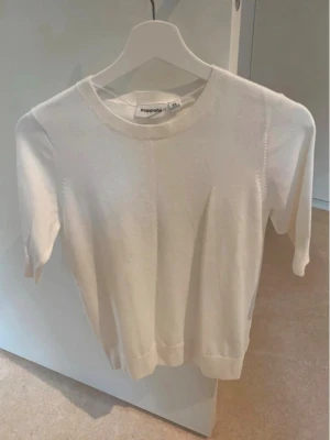 Vit stickad tröja från Kappahl - En enkel och stilren vit stickad tröja från Kappahl. Tröjan har rund halsringning, raka ärmar och ribbade muddar vid ärmslut och nederkant. Perfekt att matcha med jeans eller kjol för en clean look.