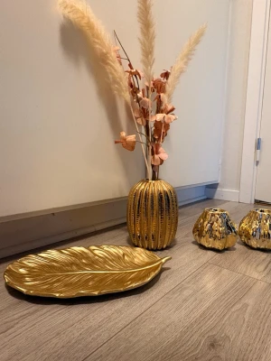 Guldigt dekorationsset med vas och fat - Skriv gärna till mig om ni bara vill ha en sak, och kom med prisförslag’Snyggt set med guldfärgad vas i rundad form, konstgjorda beige pampasgräs och rosa blommor, två guldfärgade ljuslyktor samt ett dekorativt fat i form av ett blad. Perfekt för att piffa upp rummet med lyxig känsla och trendiga detaljer.