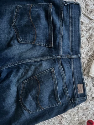 Mörkblå jeans från Lee - Snygga mörkblå jeans från Lee med klassiska bakfickor och kontrastsömmar. Modellen har normal midja och bälteshällor. Materialet är stretchigt för extra komfort och passform. Perfekta för dig som gillar en tidlös jeanslook.