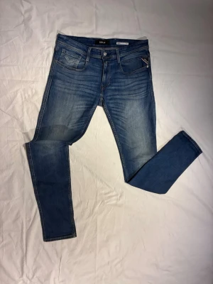 Replay Anbass - Snygga och trendiga blå slim fit jeans från Replay med klassisk femficksdesign och ljusa slitningar framtill. Jeansen har normal midja, dragkedja och knappstängning samt Replay-lapp bak i midjan. Perfekta för en avslappnad och trendig look. För mig som är 186 cm lång och väger 73,5 kg är jeansen lite väl stora i midjan. Storlek: W33 L34 | Skick 9,5/10 | Pris: 35€.
