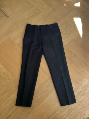 Mörkblå kostymbyxor i linneblandning med pressveck från Filippa K - Snygga mörkblå kostymbyxor från Filippa K med klassiskt rakt ben och pressveck. Tunna byxor i linneblandning som passar perfekt när det är lite varmare. Byxorna har hällor för skärp, två sidofickor fram och två passpoalfickor bak. Perfekta för en stilren och uppklädd look.