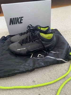 Nike Mercurial Zoom fotbollsskor - Säljer ett par Nike Mercurial Zoom fotbollsskor i svart med detaljer i neonlime. Skorna har snörning, låg profil och är tillverkade i syntetmaterial för bra grepp och känsla på planen. Perfekta för dig som vill ha snabbhet och kontroll på konstgräs eller gräs.