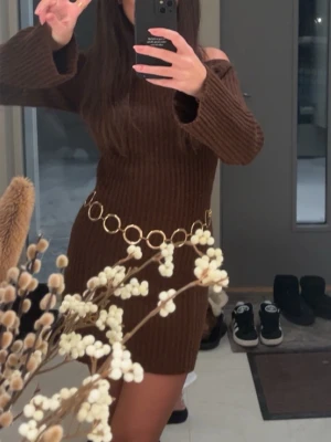 Brun ribbad offshoulder klänning - Säljer en brun kort ribbad klänning med offshoulder-design och långa ärmar. Med  Klänningen så får man en snygg guldfärgad kedja i midjan som detalj. Köpte den utan bältet men säljer den med bältet. Perfekt för dig som vill ha en trendig och bekväm look.