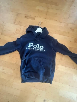 Mörkblå hoodie Polo Ralph Lauren - Snygg mörkblå hoodie från Polo Ralph Lauren med stor vit logga. Perfekt inför hösten och  perfekt för en avslappnad och trendig stil. 