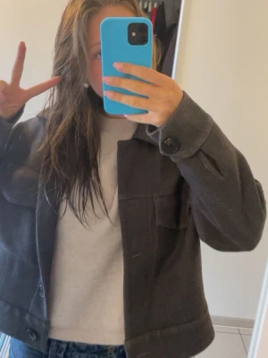 Mörkgrå kappa från InWear - Snygg mörkgrå kappa från InWear med klassisk krage, stora bröstfickor och knappar framtill. Kappan har en rak passform och är tillverkad i ett tjockare material som passar perfekt till lager på lager. Stilsäker och enkel att matcha med olika outfits.