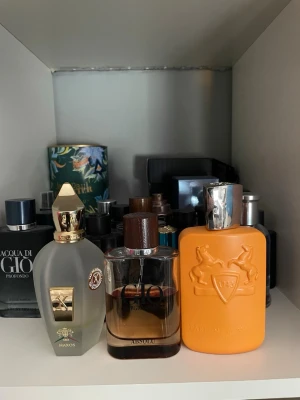 Parfymflaska i orange med silverlock - Snygg parfymflaska i matt orange med silverfärgat lock. Flaskan har en unik design med två upphöjda hästar och en sköld med siffran 1743 på framsidan. Perfekt för dig som gillar exklusiva och iögonfallande dofter.