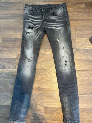 Dsquared2 jeans - Säljer ett par grå Dsquared jeans med slitningar och hål på båda benen. Jeansen har en tvättad look med ljusare partier och klassisk femficksdesign. Perfekta för en avslappnad och trendig stil.
