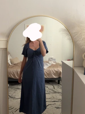 Blå långklänning med knyt framtill - Säljer en blå långklänning med korta puffärmar och knyt framtill vid bysten. Klänningen har en mjuk och flowy passform, perfekt för varma dagar. Materialet känns lätt och bekvämt mot huden.