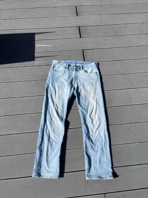 Ljusblå Levi's Premium jeans 501 - Säljer ett par ljusblå Levi's Premium jeans i klassisk rak modell. Jeansen har fem fickor, gylf med knapp och dragkedja samt snygga slitningar för en avslappnad look. Perfekta till vardags för en tidlös stil.