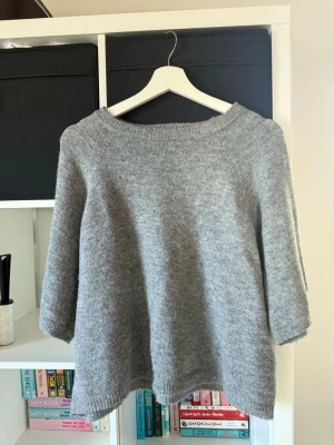 Grå stickad tröja från 157 - Mysig grå stickad tröja från 157 med rund halsringning och trekvartsärmar. Tröjan har en avslappnad passform och ribbade kanter vid hals, ärmslut och nederkant. 