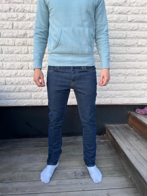 Mörkblå slim fit jeans herr - Säljer ett par mörkblå slim fit jeans med klassisk femficksdesign och kontrastsömmar. Jeansen har normal midja och raka ben, tillverkade i ett stretchigt denimtyg för skön passform. Perfekta för dig som gillar en enkel och stilren look. Storlek 29/30