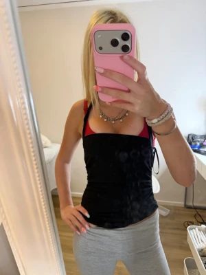 Svart och röd linnetopp - Säljer en svart linnetopp med röda axelband och detaljer. Toppen är tight och har en enkel, stilren design som passar perfekt till jeans eller kjol. Materialet känns mjukt och stretchigt, vilket gör den bekväm att bära hela dagen.