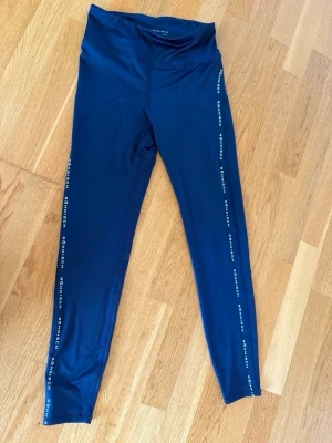 Blå leggings från Röhnisch - Snygga blå leggings från Röhnisch med logga längs sidorna. De har hög midja och är tillverkade i ett stretchigt, mjukt material som passar perfekt till träning eller chill. Tight passform. Aldrig använda 