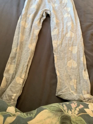 Gråa pyjamasbyxor med vita hjärtan - Mysiga pyjamasbyxor i ljusgrått med vita hjärtmönster. Byxorna har en avslappnad passform och är gjorda i ett mjukt och tunt material, perfekt för chillkvällar hemma. Elastisk midja för extra komfort.