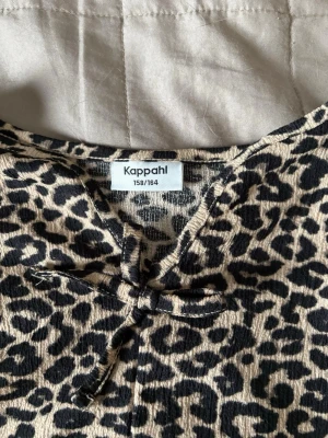 Leopardmönstrad blus från Kappahl - Snygg blus från Kappahl, aldrig använd, i leopardmönster med beige botten och svarta fläckar. Blusen har långa ärmar, v-ringning med knytband och lätt rynkad nederdel. Perfekt för dig som gillar djurmönstrat och vill sticka ut.