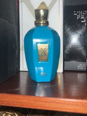Xerjoff Eau de Parfum 100ml - Lyxig parfym från Xerjoff i en elegant turkos flaska med gulddetaljer. Flaskan har en sexkantig form och kommer i en stilren vit förpackning med gulddetaljer och stor X-logga. Eau de Parfum med exklusiv känsla, tillverkad i Italien.