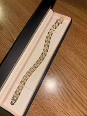 Guldarmband med gnistrande stenar - Snyggt armband i guldton med massor av små, runda briljantslipade stenar som ger ett riktigt lyxigt intryck. Armbandet har ett elegant mönster och kommer i en stilren ask. Perfekt för dig som vill sticka ut med accessoarer som glittrar.