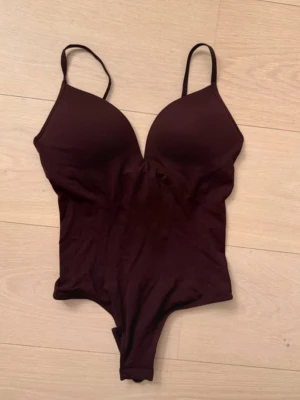 Vinröd trendy body push up med smala axelband - Snygg vinröd snatching shapewear body med tunna axelband och vadderade kupor. Bodyn har en djup urringning och är tillverkad i ett stretchigt, mjukt material som sitter skönt mot kroppen. Perfekt för att skapa en clean och stilren look. Storlek m men passar S!