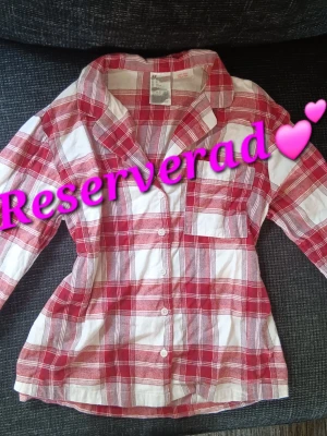 pyjamas set - Klassisk tvådelad pyjamas med långärmad skjorta och byxor i rödvitt rutigt mönster. Skjortan har krage, bröstficka och knappar framtill. Byxorna har dragsko i midjan för extra komfort. Perfekt till jul och mysiga kvällar.