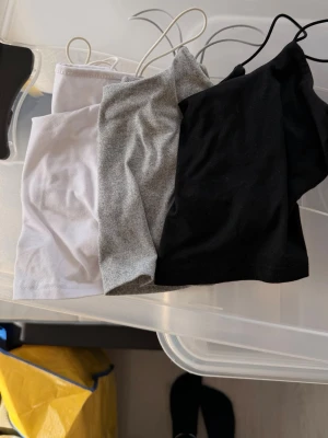 3-pack croppade linne-toppar - Säljer ett 3-pack croppade linne-toppar i vitt, grått och svart. Alla toppar är ärmlösa med tunna axelband och har en enkel, stilren design. Perfekta att matcha till olika outfits och superbekväma tack vare mjukt bomullsmaterial.