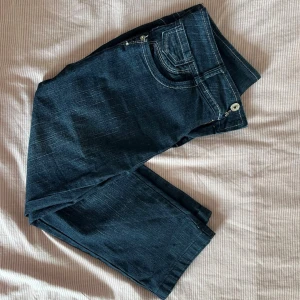 Mörkblå raka jeans capris med vita sömmar - Snygga mörkblå jeans med raka ben och kontrasterande vita sömmar. Klassisk femficksmodell med dragkedja och knapp framtill. Jeansen har en stilren look och passar perfekt till en avslappnad outfit.
