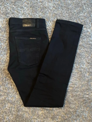 Nudie Jeans-Lean Dean  - Säljer ett par svarta slim jeans från Nudie i modellen Lean Dean och färgen Everblack med klassisk femficksmodell. Jeansen har en slim passform. Använda ett fåtal gånger. Köpta nya från nudies butik i Götet. Perfekta för en stilren och modern look. Storlek W31 & L32 