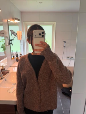 Brun fluffig kofta med v-ringning - Mysig brun kofta med v-ringning och lång ärm. Koftan har en fluffig, mjuk struktur och en avslappnad passform. Perfekt att slänga på sig över en t-shirt eller topp för en chill look.