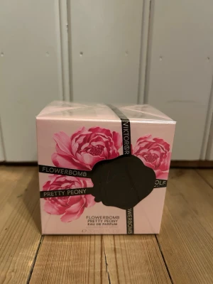 Flowerbomb Pretty Peony parfym - Flowerbomb Pretty Peony Eau de Parfum från Viktor & Rolf. Förpackningen är ljusrosa med stora rosa pionblommor och svarta banddetaljer. En feminin och blommig doft i elegant designad kartong, perfekt för dig som älskar fräscha och romantiska parfymer.
