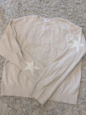 Beige stickad tröja med stjärnor - Säljer en beige stickad tröja med vita stjärnor på ärmarna. Tröjan har rund halsringning, långa ärmar och ribbade muddar. Perfekt för dig som gillar en enkel men ändå unik look. Jätteskönt material, jättegullig och fint skick! 💖