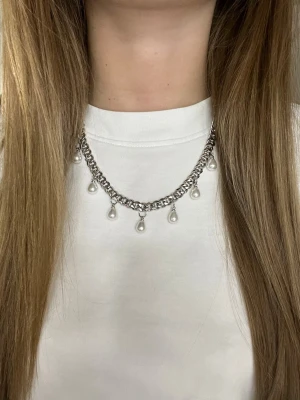 Silverfärgat halsband med pärldroppar - Snyggt halsband i silverfärgad metall med kedja och hängande vita pärldroppar. Kedjan har en chunky känsla och pärlorna ger en elegant touch. Perfekt för att lyfta vilken outfit som helst. Rostfritt stål och handgjort 