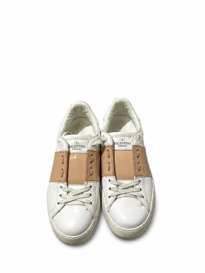Valentino sko - Snygga vita sneakers från Valentino med bred beige läderdetalj över snörningen och coola nitar på hälen. Skorna har klassisk låg profil och är tillverkade i läder för en lyxig känsla. Perfekta för dig som vill sticka ut med stilrena detaljer.