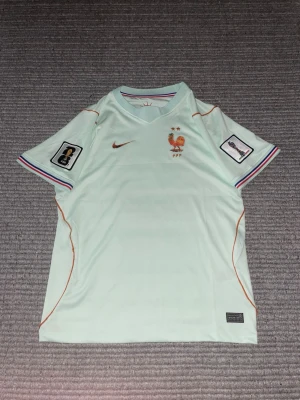 Nike fotbollströja Frankrike Mint - Snygg fotbollströja från Nike med Frankrikes landslagsemblem och två stjärnor på bröstet. Tröjan har korta ärmar, orangea sömmar och färgglada detaljer vid ärmsluten. Tillverkad i lätt och ventilerande material, perfekt för träning eller match.