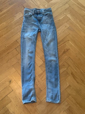 Ljusblå slim fit  jeans nudie - Säljer ett par ljusblå slim fit jeans med klassisk femficksdesign och normalhög midja. Jeansen har slitningar och tvättade detaljer för en avslappnad look. Dem är från nudie nudie, Str w27 L32. Nypris är 1600kr och mitt pris är 499kr. Dem är inte använda mycket 