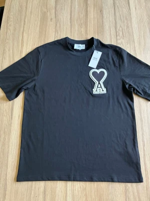 Ami Paris t-shirt - Snygg svart t-shirt från Ami med en stor broderad hjärtdetalj och bokstaven A på bröstet. Klassisk rund halsringning och korta ärmar. Tillverkad i mjuk bomull för skön känsla och stilren look.